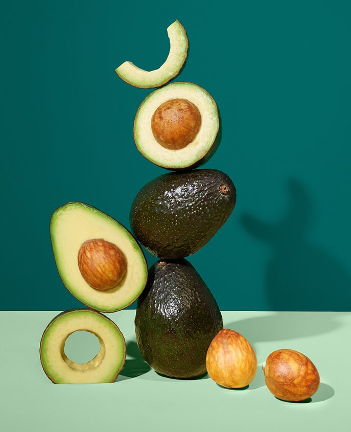 A creative display of avocados artistically stacked on a two-tone background with the text 'OUR CLEAN COMMITMENT'